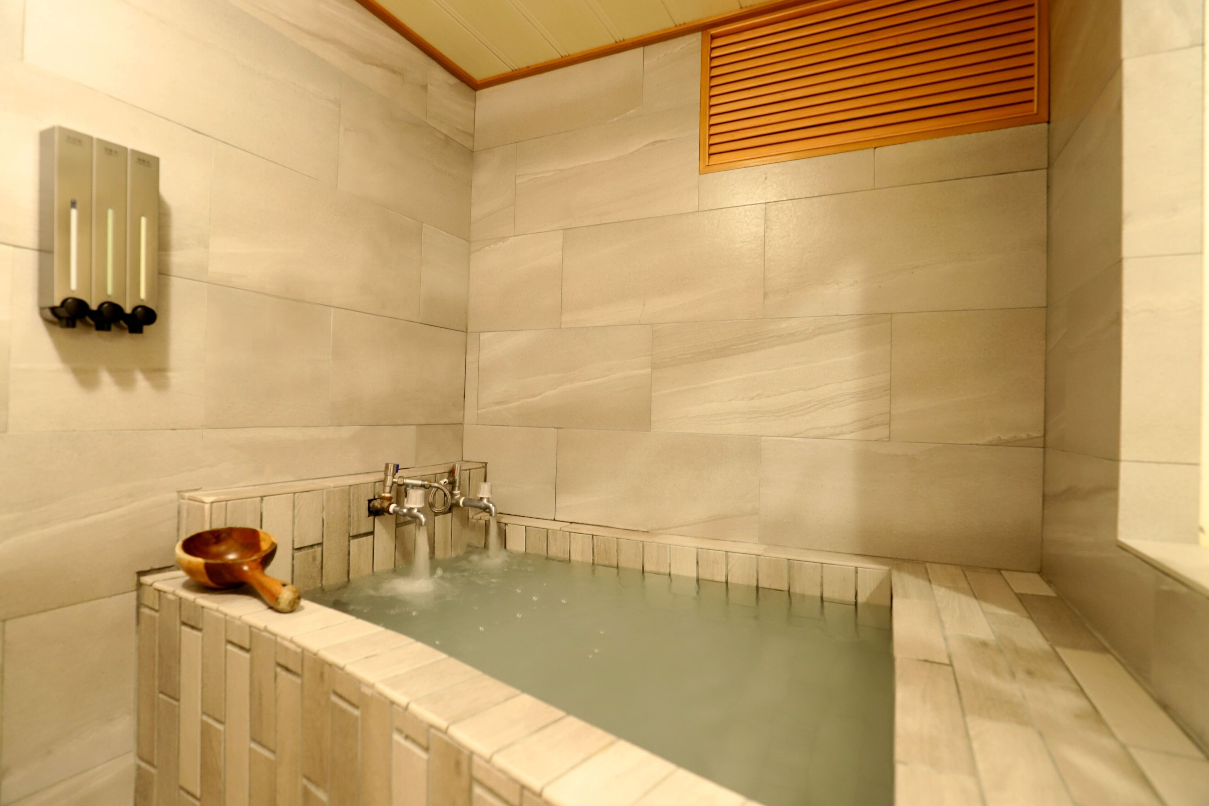 A modern bathroom with a freestanding bathtub, a wooden bowl, and a wall-mounted hand dryer.