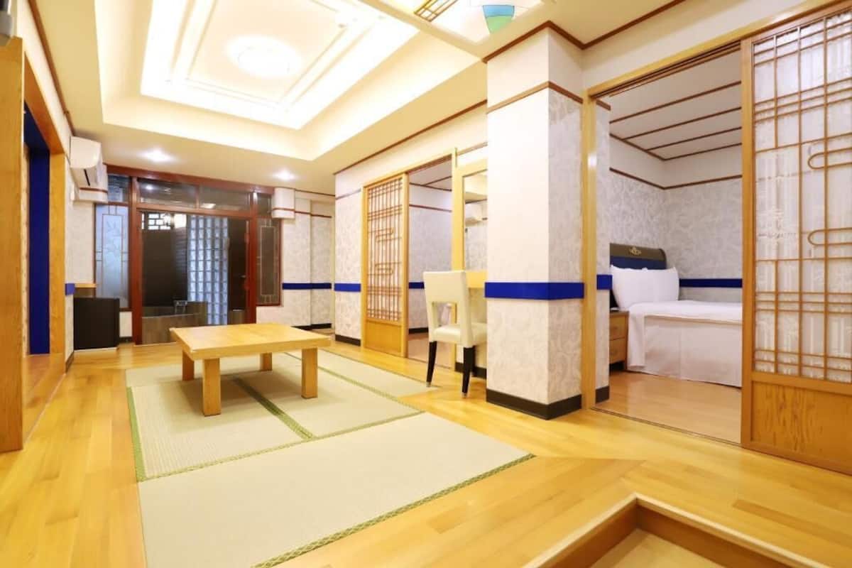 A traditional Japanese-style room with tatami flooring, a low wooden table, a bed with a white bedspread, and a sliding door with a decorative screen.