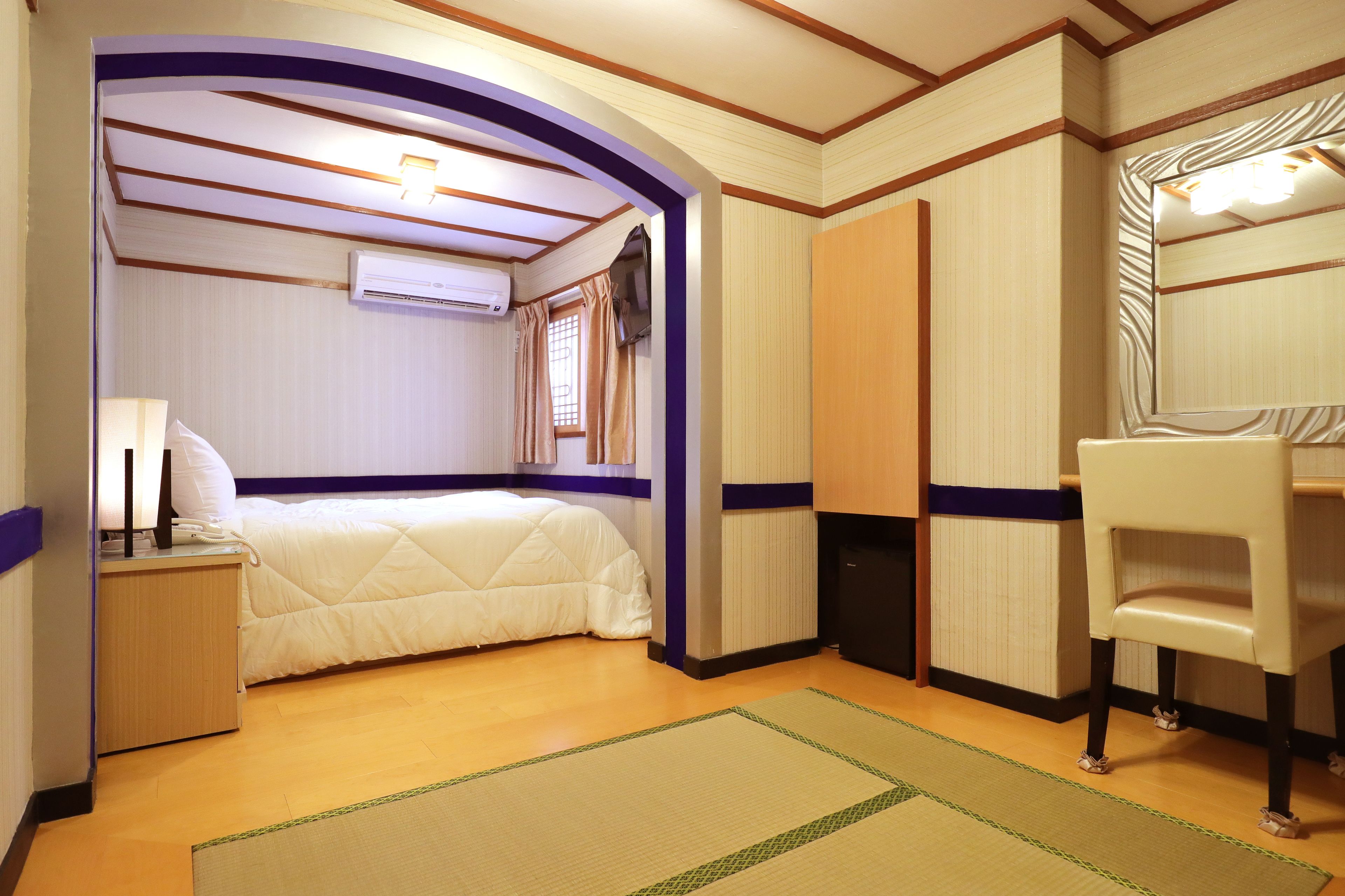 A hotel room with a bed, a desk, a chair, a mirror, and a window with curtains.