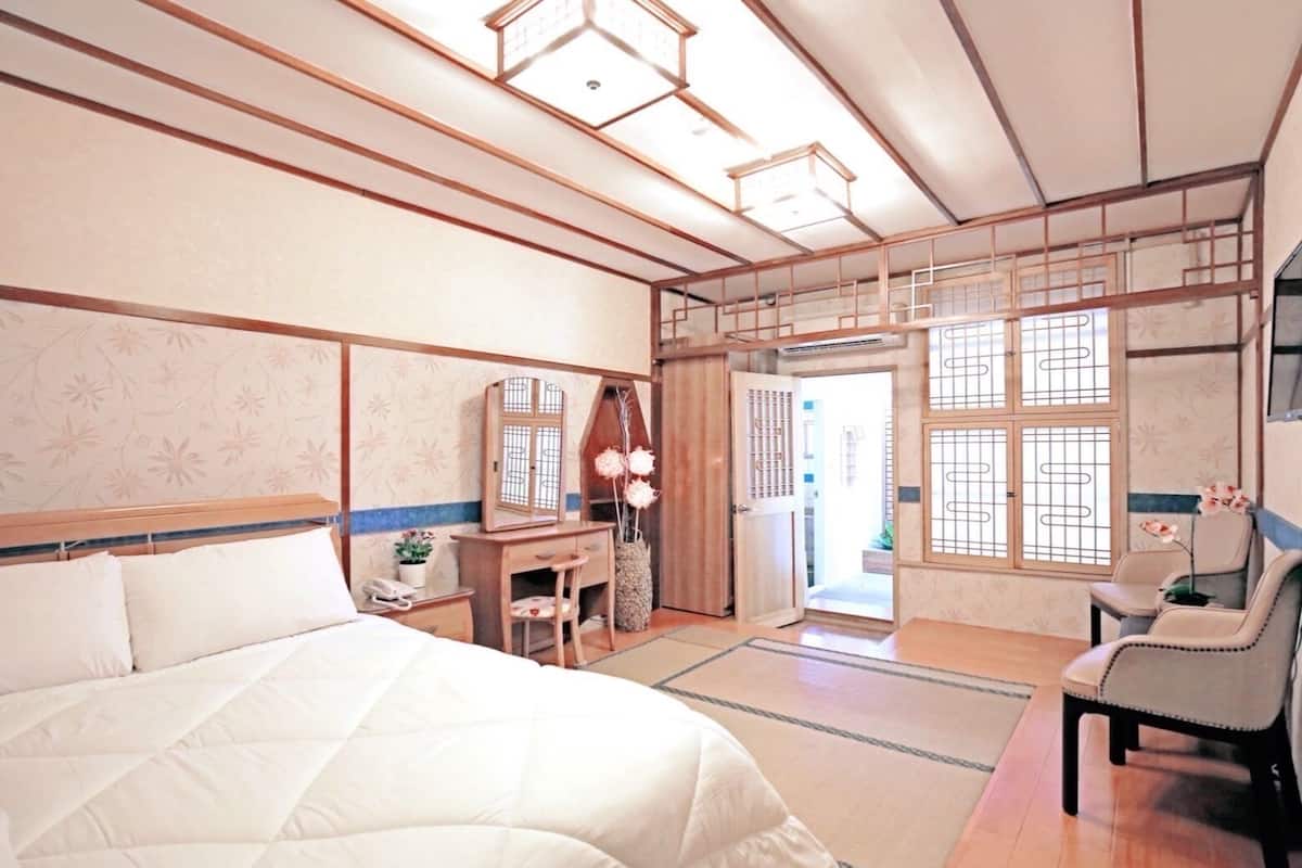 A traditional Japanese-style bedroom with tatami flooring, a large bed, a desk with a mirror, and sliding doors leading to a balcony.