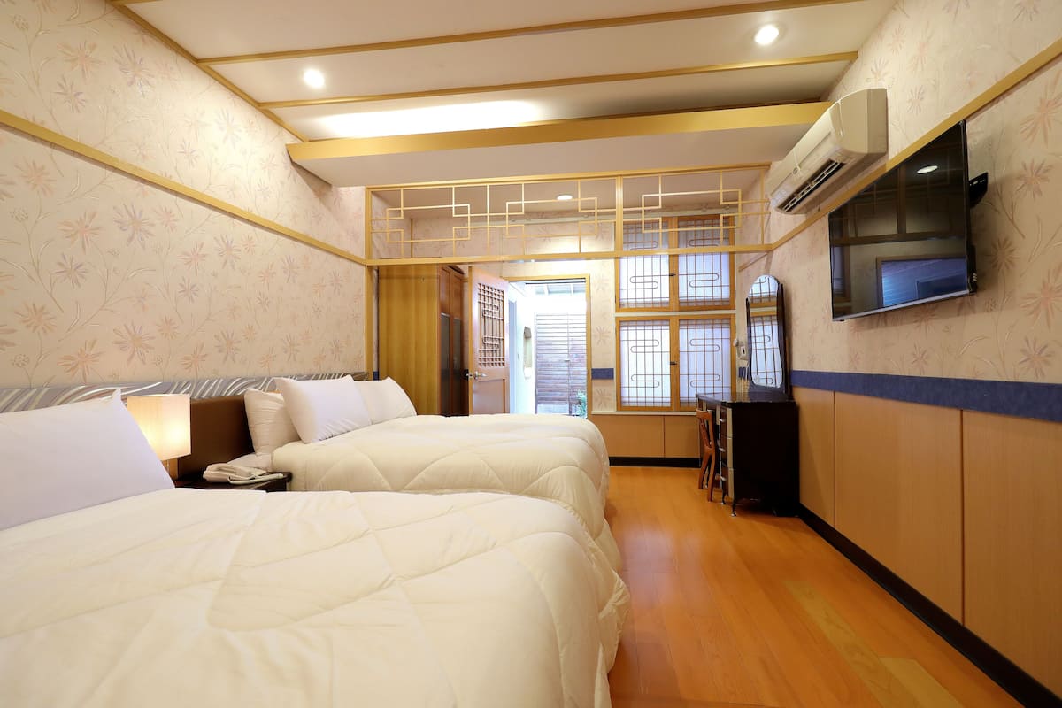 A hotel room with two beds, a TV mounted on the wall, and a wooden floor.