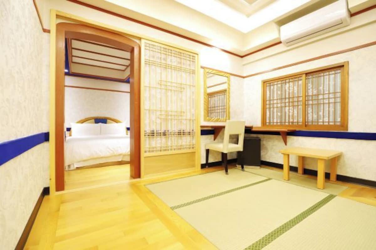 A traditional Japanese-style room with tatami flooring, a bed with a wooden headboard, a desk, and a chair.