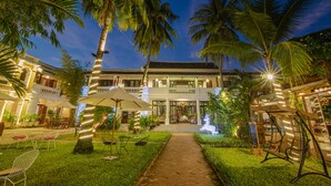 A well-lit courtyard with a pathway leading to a building with a balcony. There are outdoor seating areas and a swing chair. - Ha An Hotel (Hoi An)