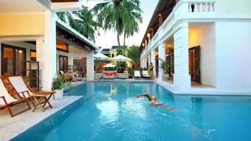 Una piscina con sillones de descanso y sombrillas, rodeada de palmeras y edificios.
