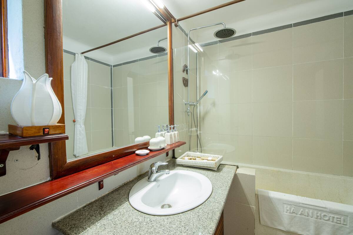Baño con lavamanos, espejo, ducha y perchero para toallas.
