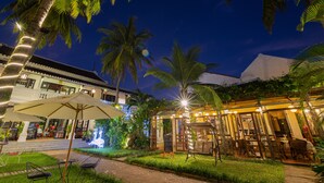 A restaurant with outdoor seating, palm trees, and a well-lit patio area. - Ha An Hotel (Hoi An)