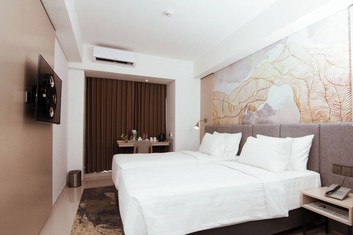 Una habitación de hotel moderna con una cama grande, un escritorio con lámpara, un televisor montado en la pared y un adorno decorativo en la pared.