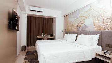 A modern hotel room with a large bed, a desk with a lamp, a TV mounted on the wall, and a decorative wall piece.
