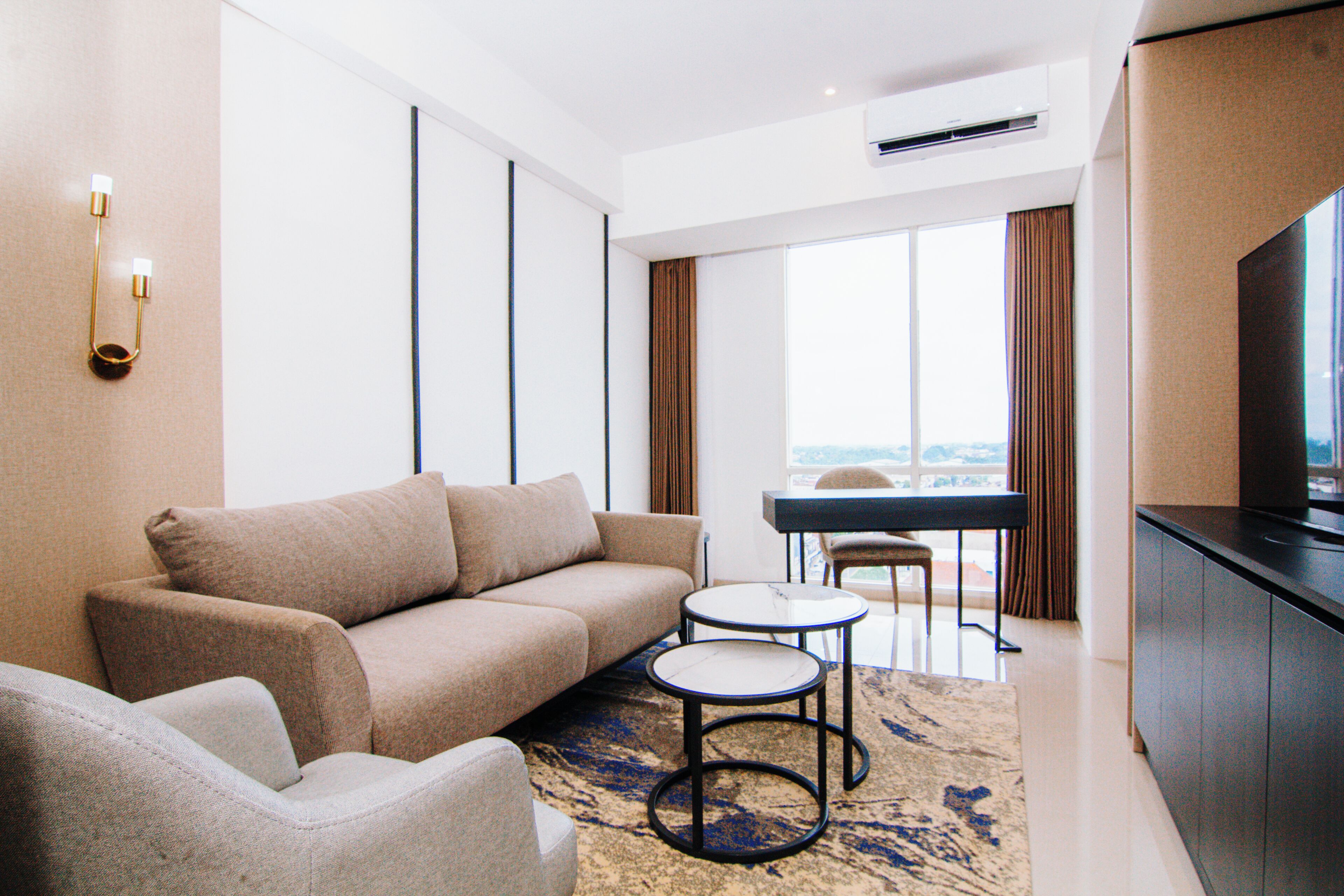 Una habitación de hotel moderna con sofá, una mesita redonda, televisión de pantalla plana y vistas a la ciudad a través de amplias ventanas.