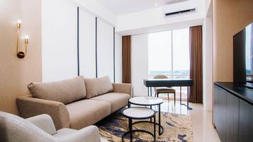 Una habitación de hotel moderna con sofá, una mesita redonda, televisión de pantalla plana y vistas a la ciudad a través de amplias ventanas.
