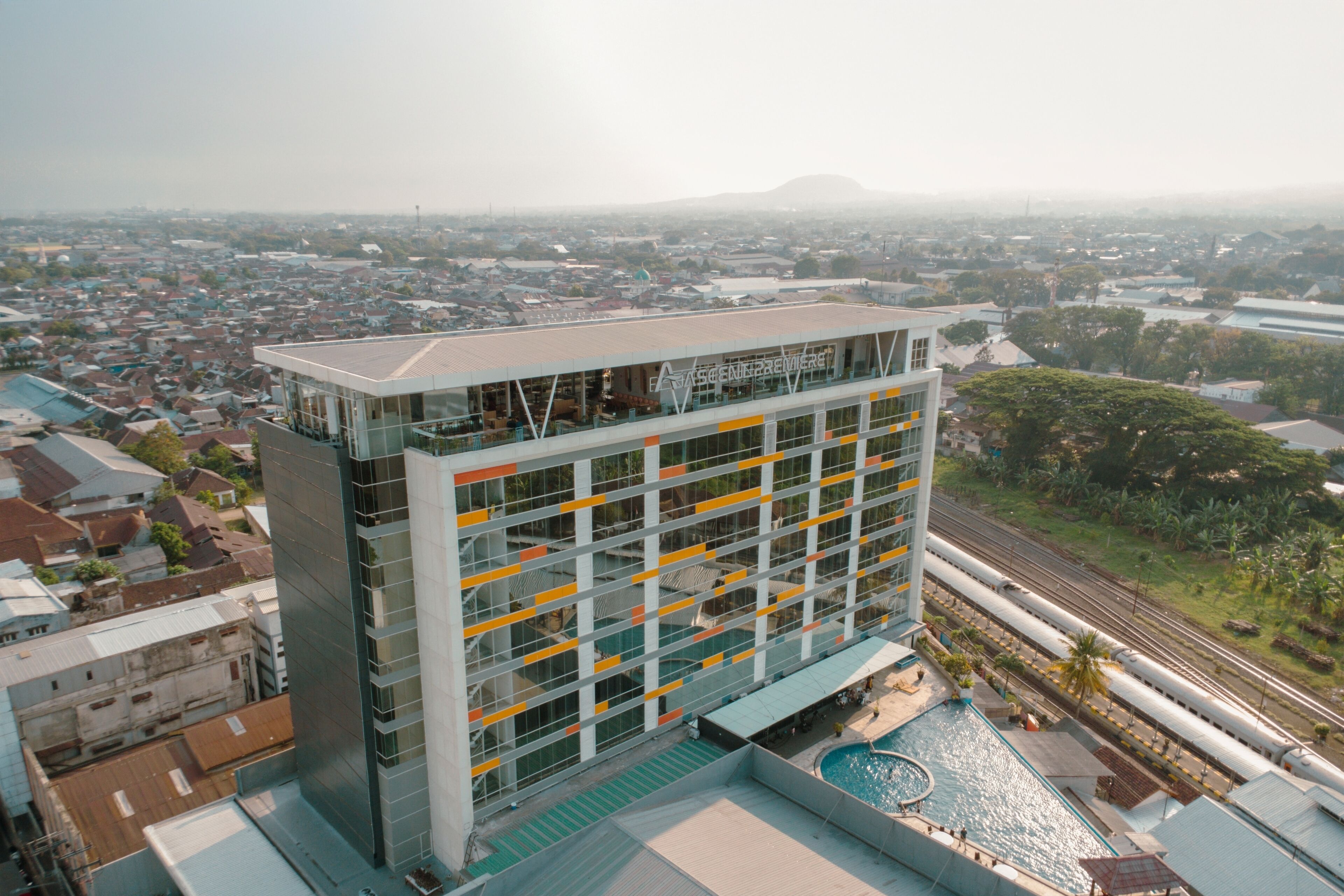 A modern hotel with a glass facade, a rooftop pool, and a view of the surrounding cityscape.