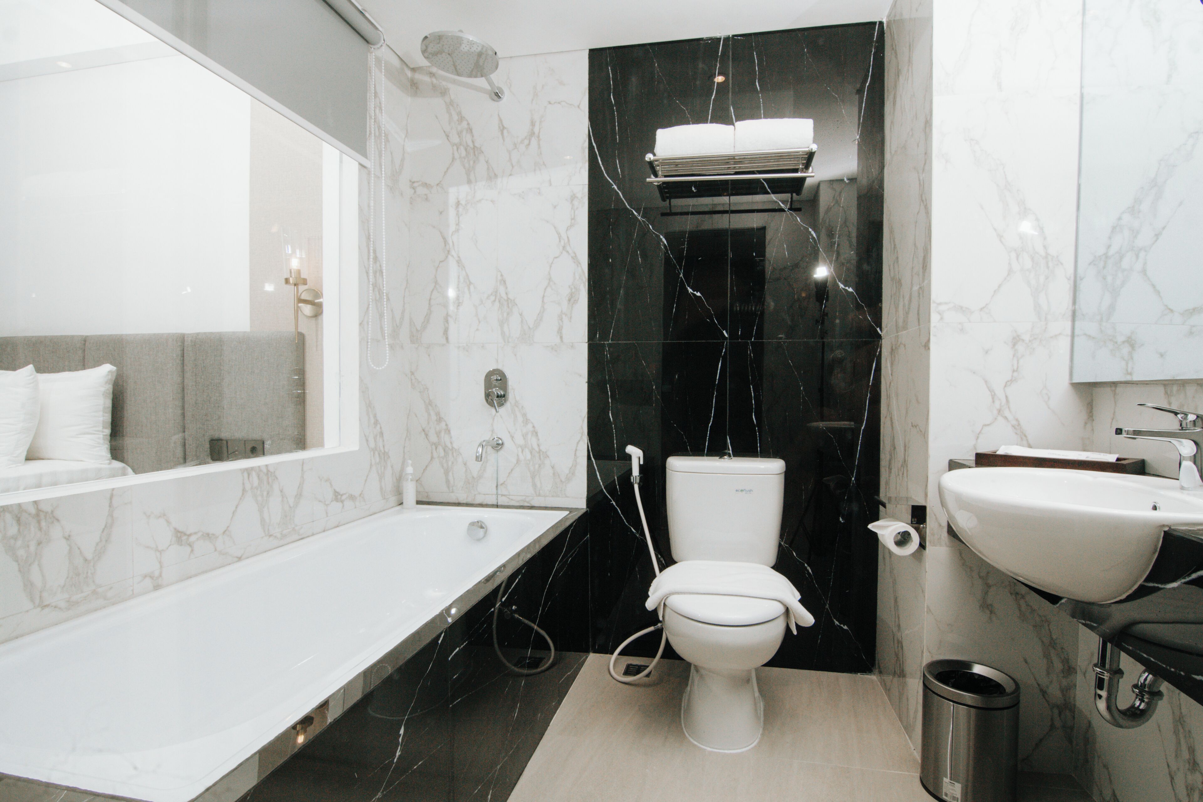 Une salle de bain moderne dotée d’une baignoire, de toilettes et d’un lavabo, avec des murs recouverts de marbre et de carreaux noirs.