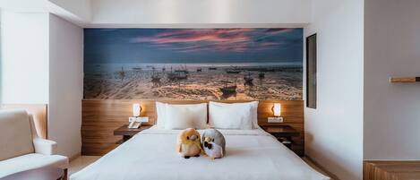 A hotel room with a large bed, two nightstands, a chair, and a painting of a beach scene on the wall.