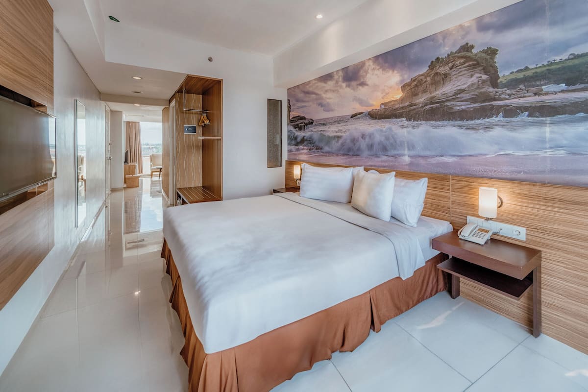 Habitación de hotel moderna con una cama grande, un televisor de pantalla plana, un cuadro de una escena costera y vistas a la ciudad.