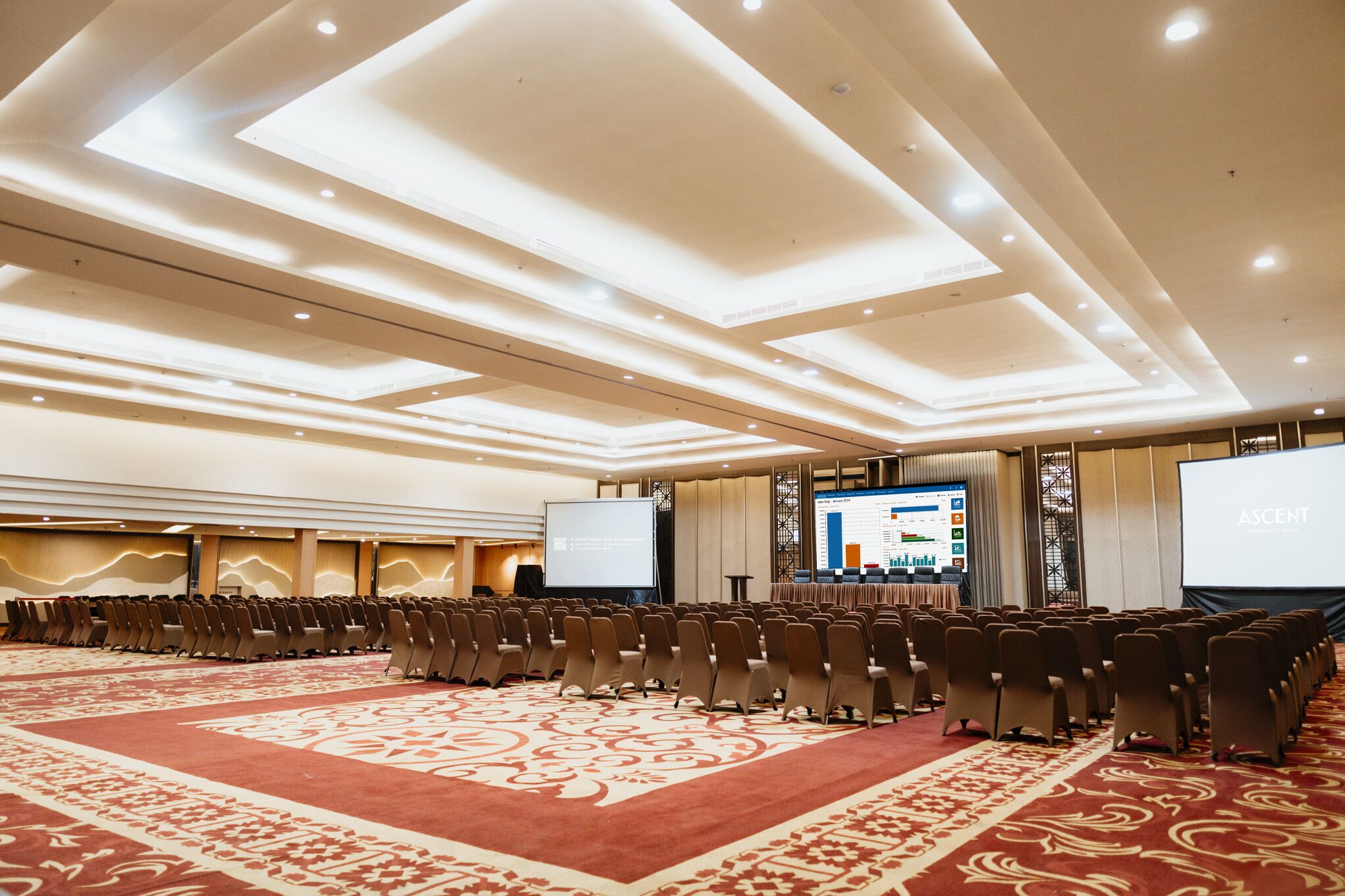 A conference room with rows of chairs, a large screen, and a presentation area.