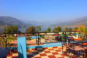 Una terraza con suelo a cuadros, mobiliario exterior y vistas a un lago y montañas.