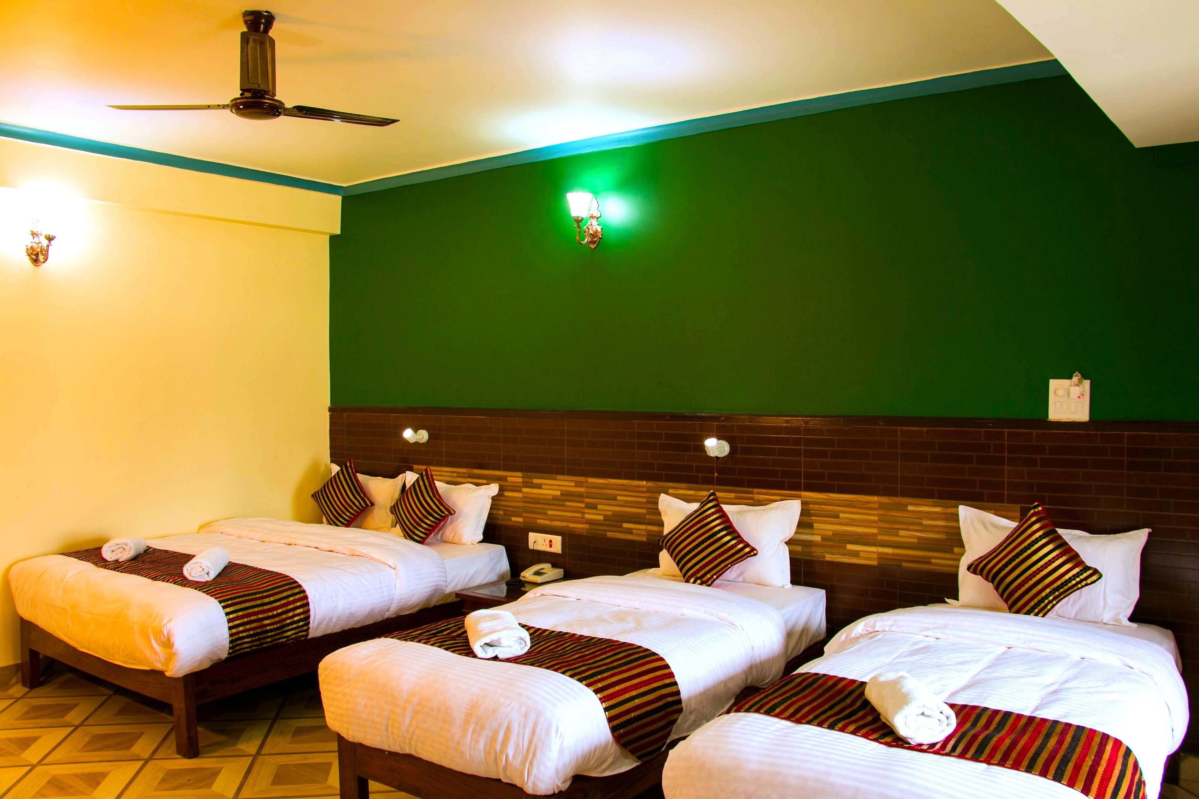 Habitación de hotel con tres camas, ventilador de techo y una pared de acento verde.