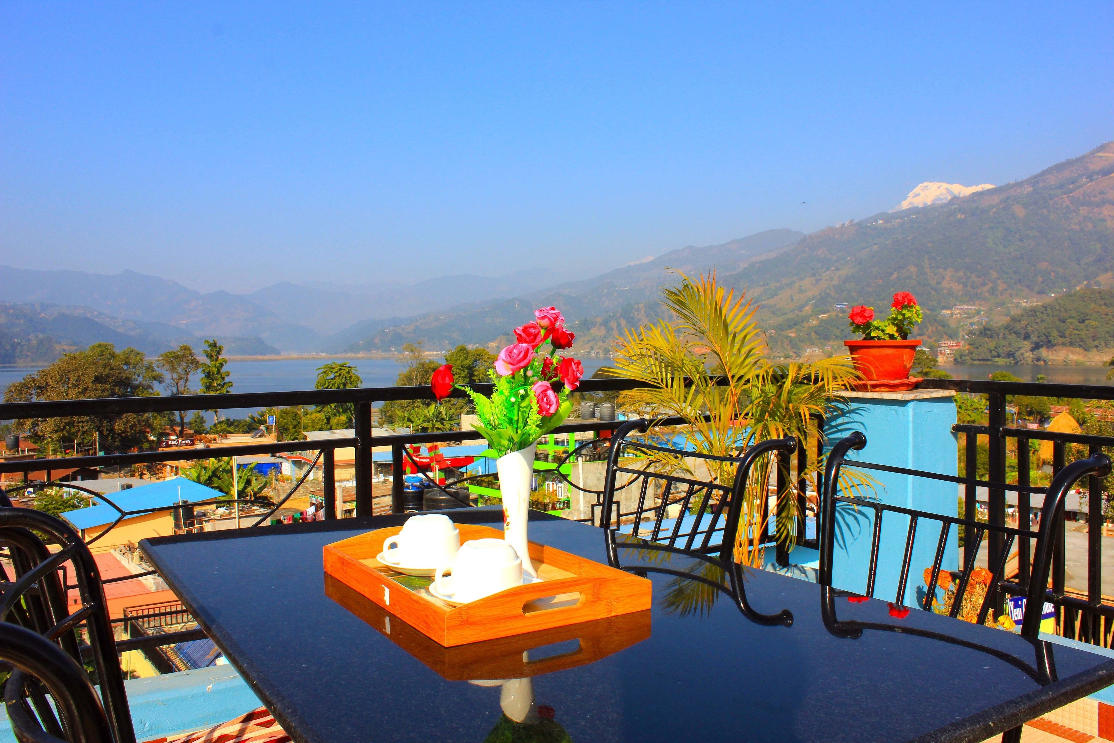 A balcony with a table, two potted plants, and a view of mountains and a lake.