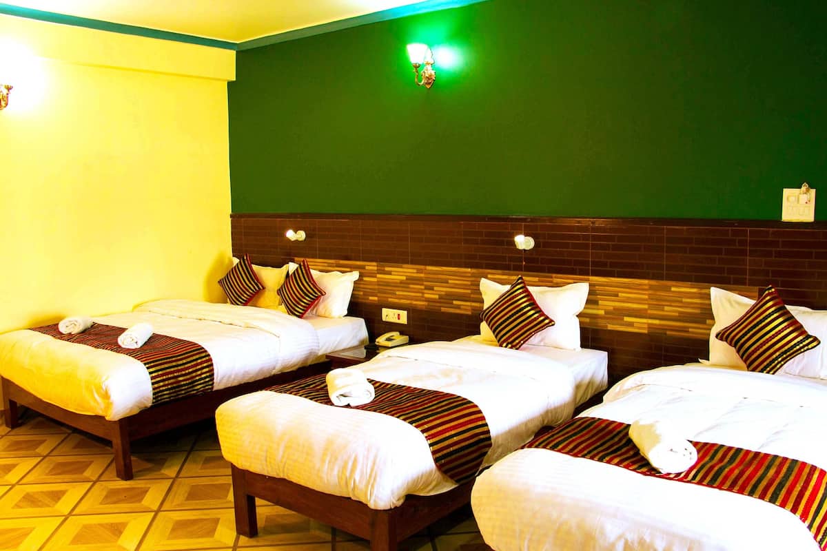 Ein Hotelzimmer mit drei Einzelbetten, jedes mit weißen Laken und gestreiften Decken. Der Raum hat eine grüne Akzentwand und ein Holz-Kopfteil.