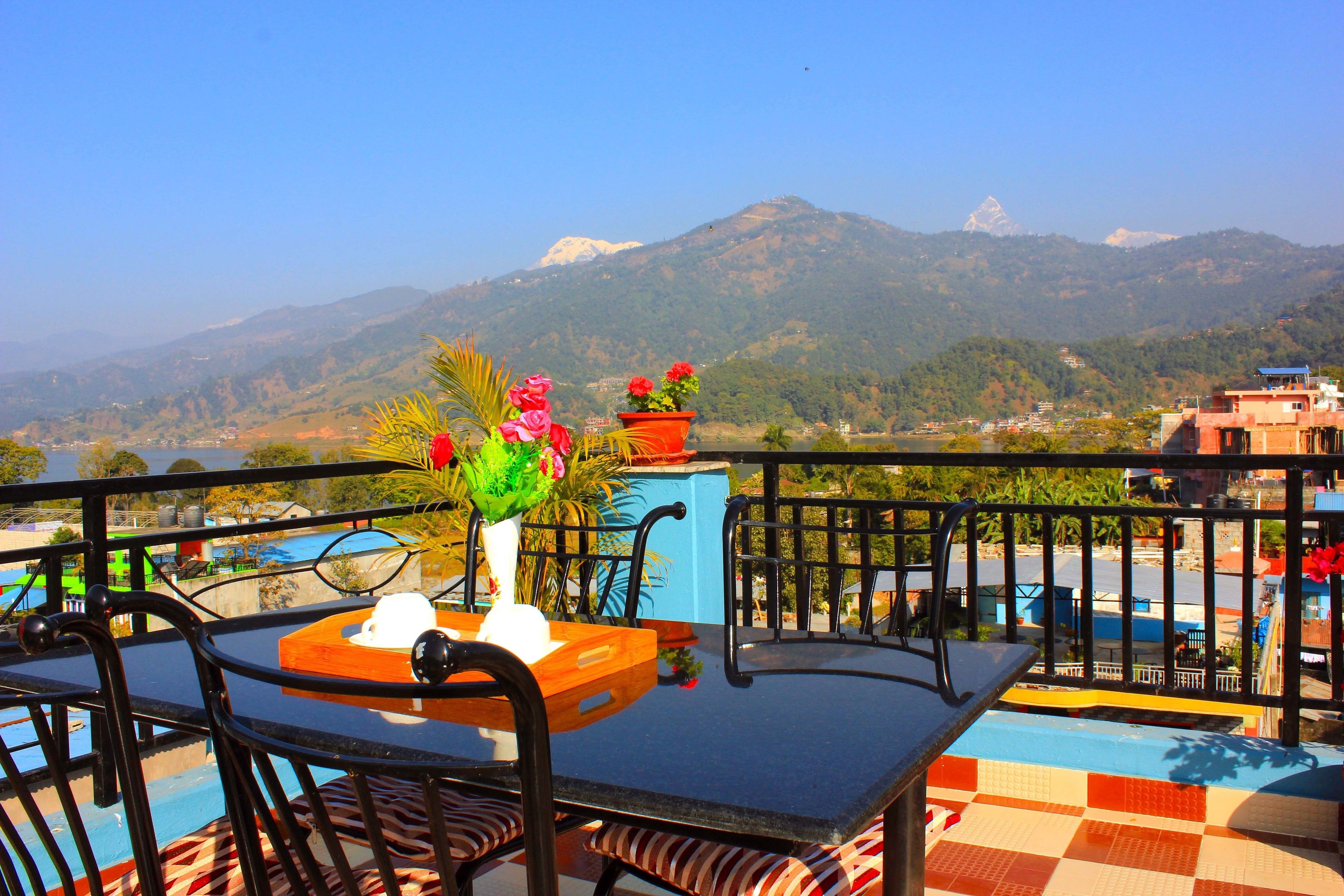 Un balcon avec une table et des chaises, un vase rempli de fleurs et une vue sur les montagnes en arrière-plan.