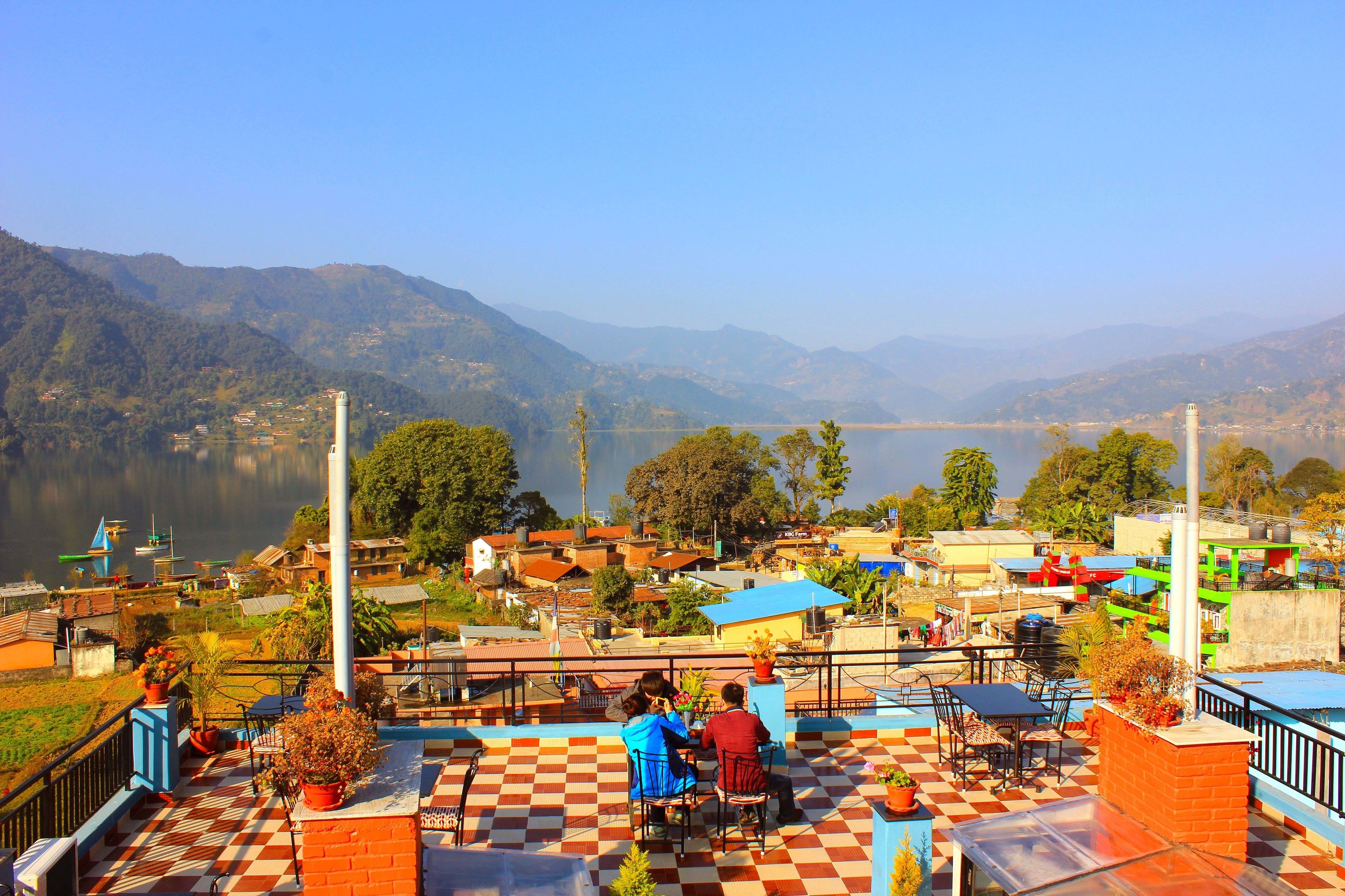 A terrace with a checkered floor, outdoor seating, and a view of a lake and mountains.