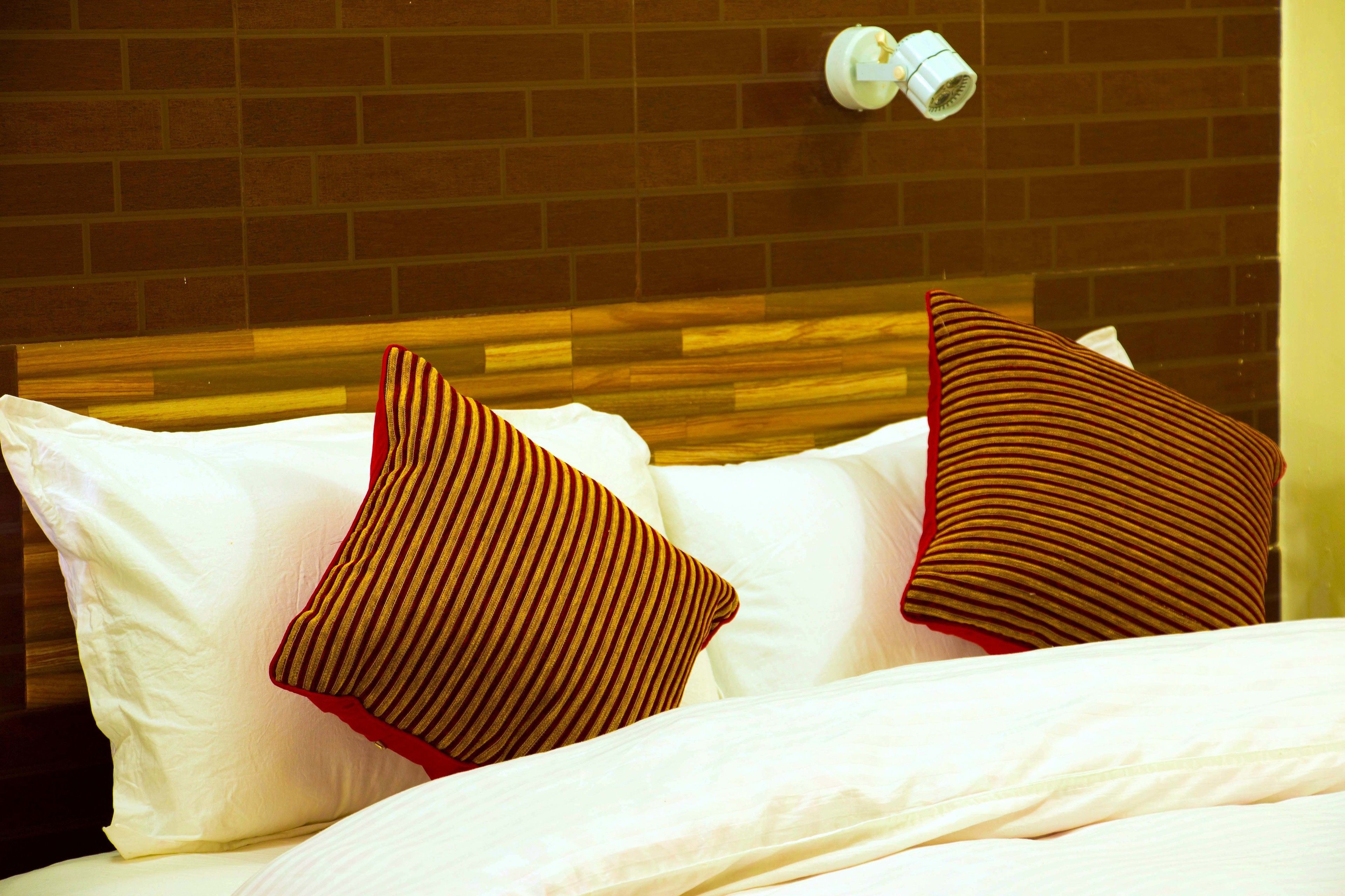 Un lit avec une literie blanche et deux coussins à rayures, un mur de briques et un objet blanc accroché au mur.