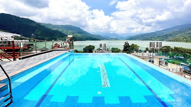 Une piscine à l’eau d’un bleu cristallin, entourée d’une terrasse et offrant une vue sur un lac et des montagnes.