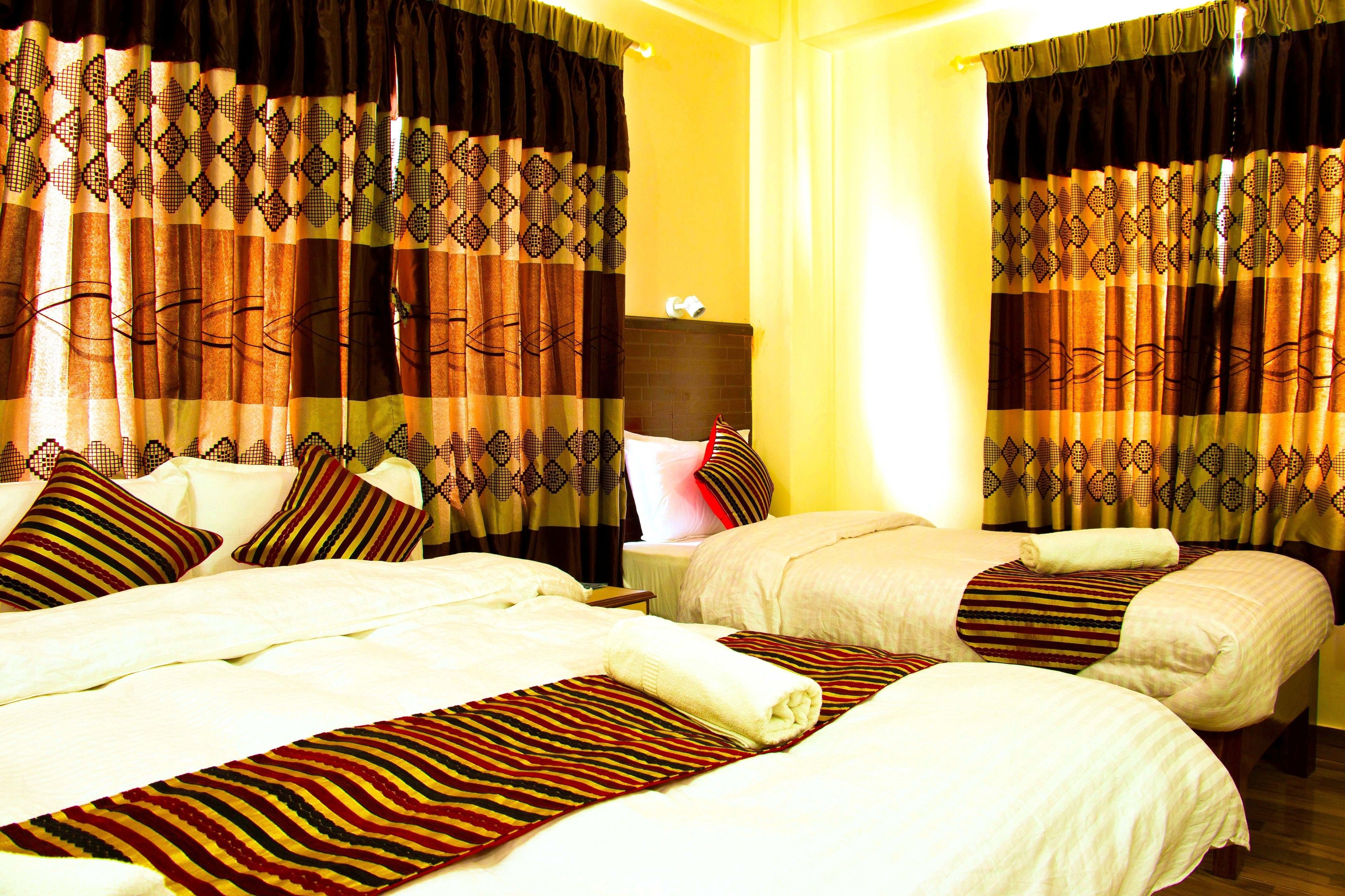 A hotel room with two beds, patterned curtains, and a bright yellow wall.
