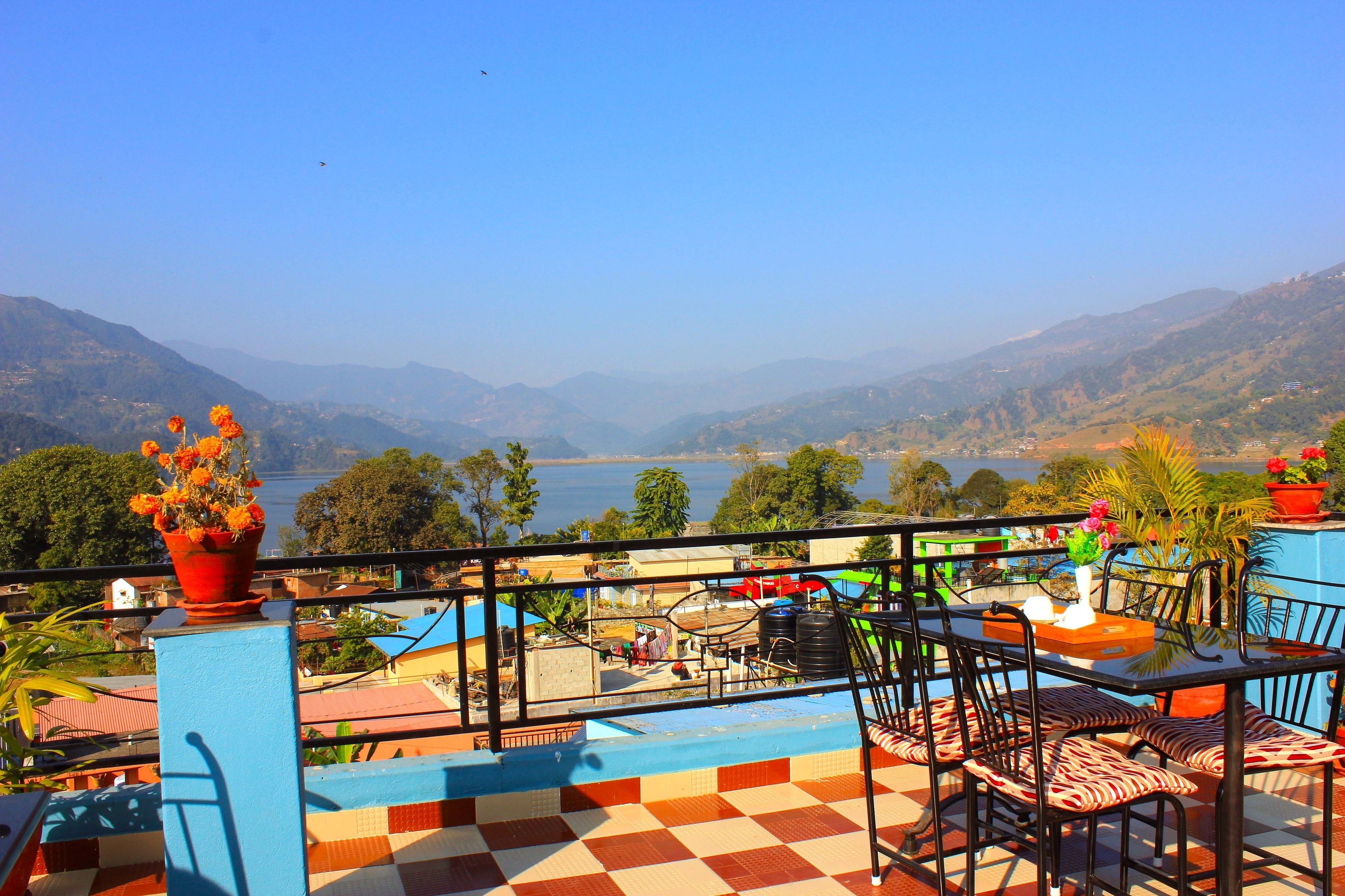 A terrace with a checkered floor, outdoor seating, and a view of a lake and mountains.