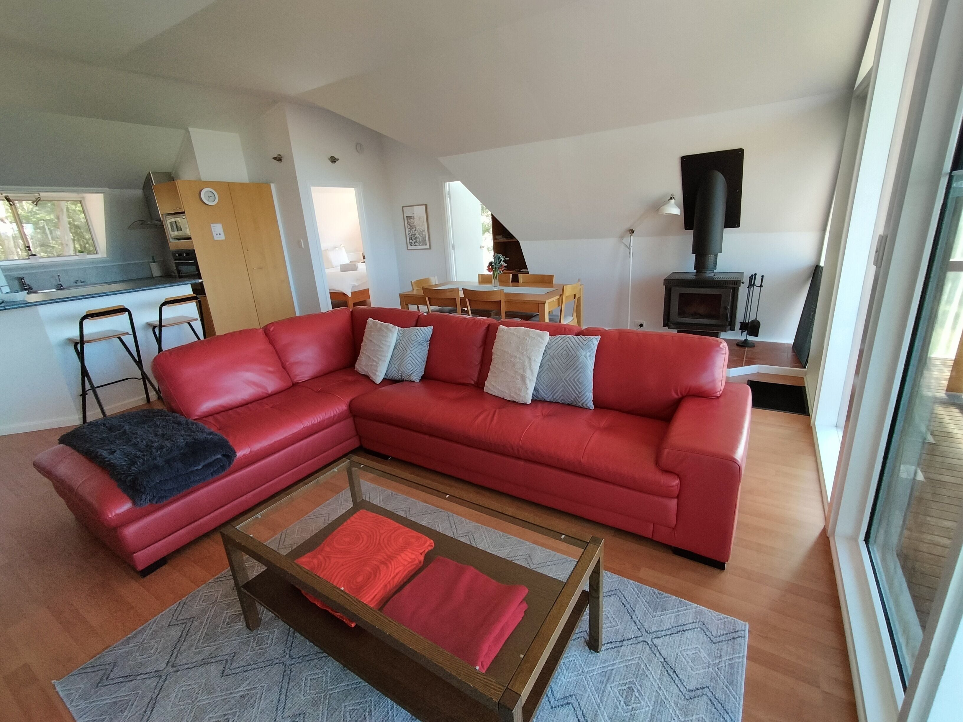 A modern living room with a red sectional sofa, a glass coffee table, and a kitchen area in the background.