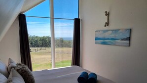 A bedroom with a large window, a bed with pillows, a painting, and a key on the wall. - Tennessee Hill Chalets (Lowlands)