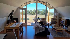 A spacious living area with a large glass door leading to an outdoor deck, a cozy seating area with a sofa and chairs, a dining table, and a bookshelf. - Tennessee Hill Chalets (Lowlands)