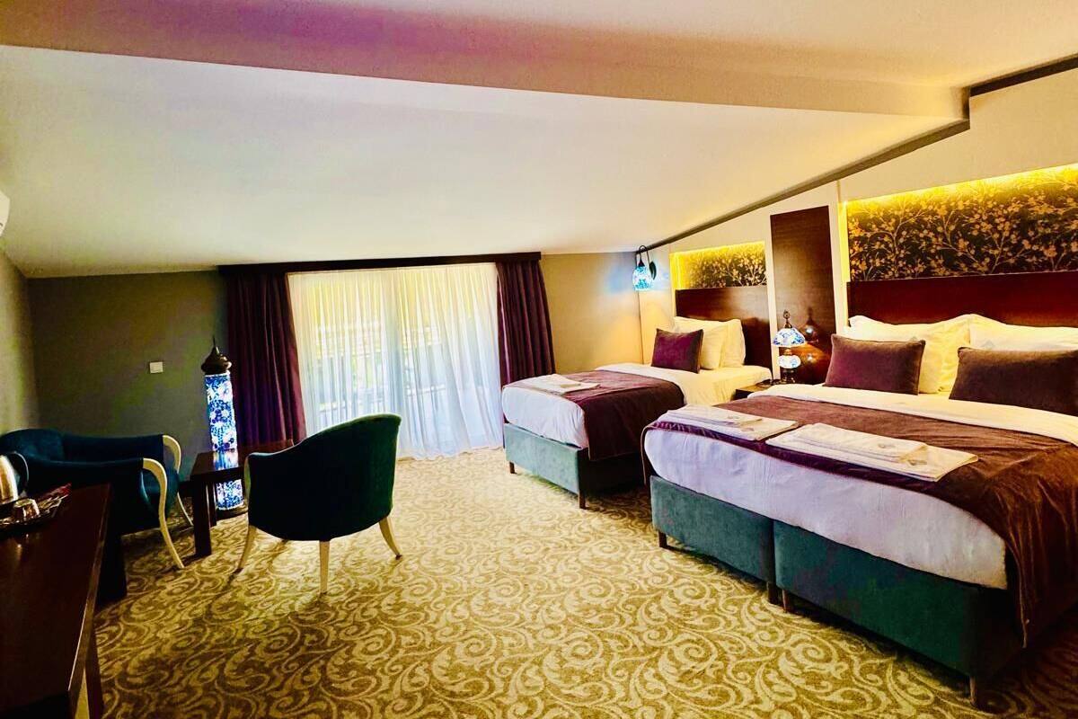 Ein Hotelzimmer mit zwei Betten, einem Schreibtisch, einem Stuhl und einem großen Fenster mit Vorhängen.