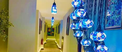 A hallway with patterned carpet, blue decorative lights, and framed artwork on the walls.