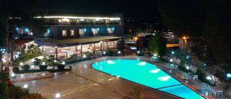 Un hotel con piscina, mobiliario exterior y un edificio bien iluminado.