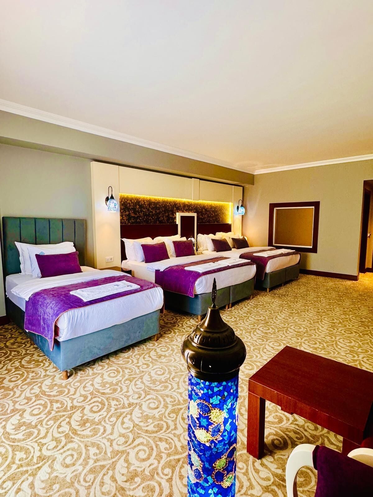 A hotel room with two beds, a TV, a decorative vase, and a patterned carpet.