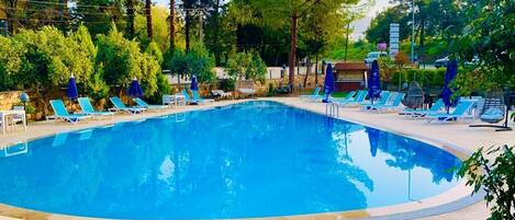 A swimming pool with lounge chairs and umbrellas, surrounded by trees.