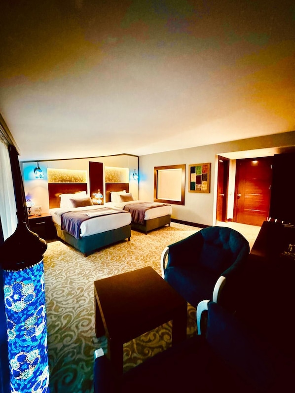 Habitación de hotel con dos camas, un área de estar con una silla, una mesita y un espejo.