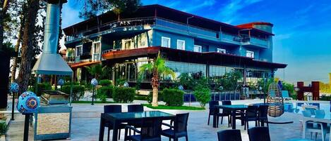 A modern building with a multi-level structure, outdoor seating area with tables and chairs, and a decorative chimney.