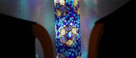 A tall, narrow, illuminated structure with a patterned design, possibly a decorative piece or a light fixture.
