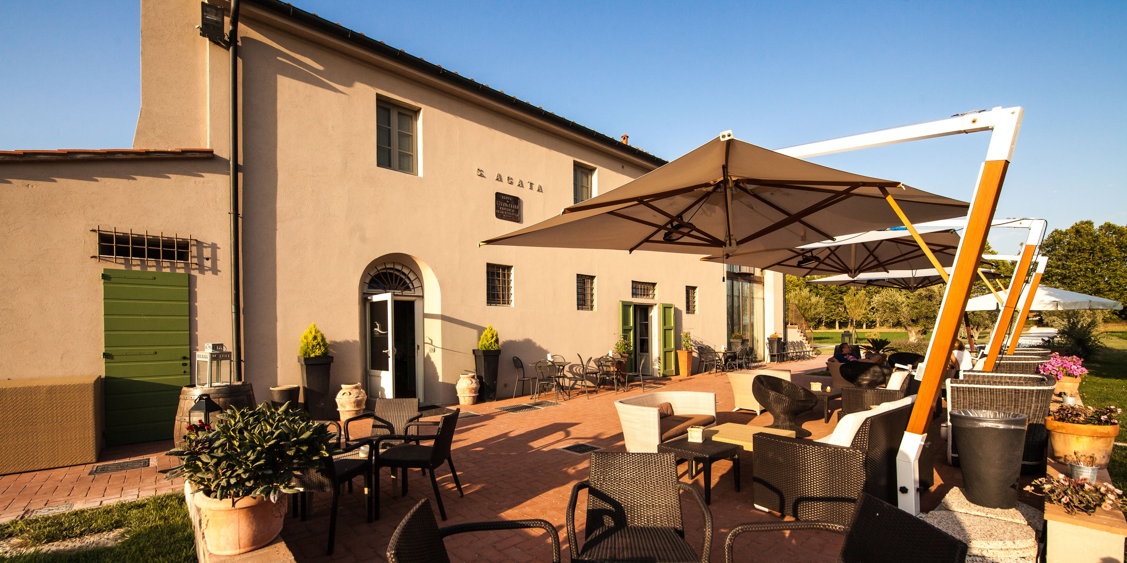 An outdoor patio area with wicker furniture, umbrellas, and potted plants.