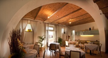 Zona pranzo con tavoli apparecchiati per un pasto, soffitto in mattoni e vista sull'esterno.