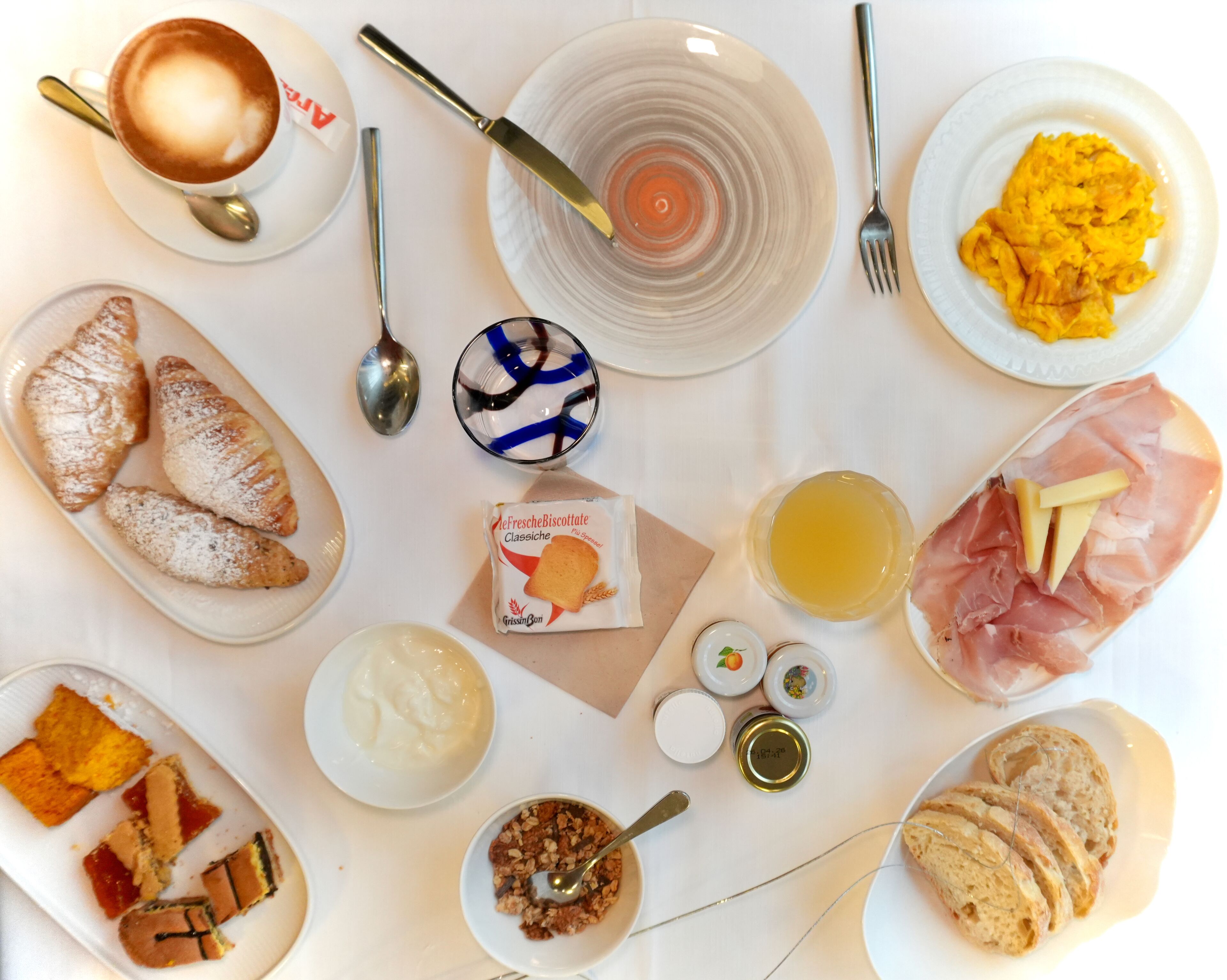 A breakfast table with croissants, scrambled eggs, ham, cheese, and various spreads.