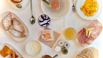 Ein Frühstückstisch mit Croissants, Rührei, Schinken, Käse und verschiedenen Aufstrichen.