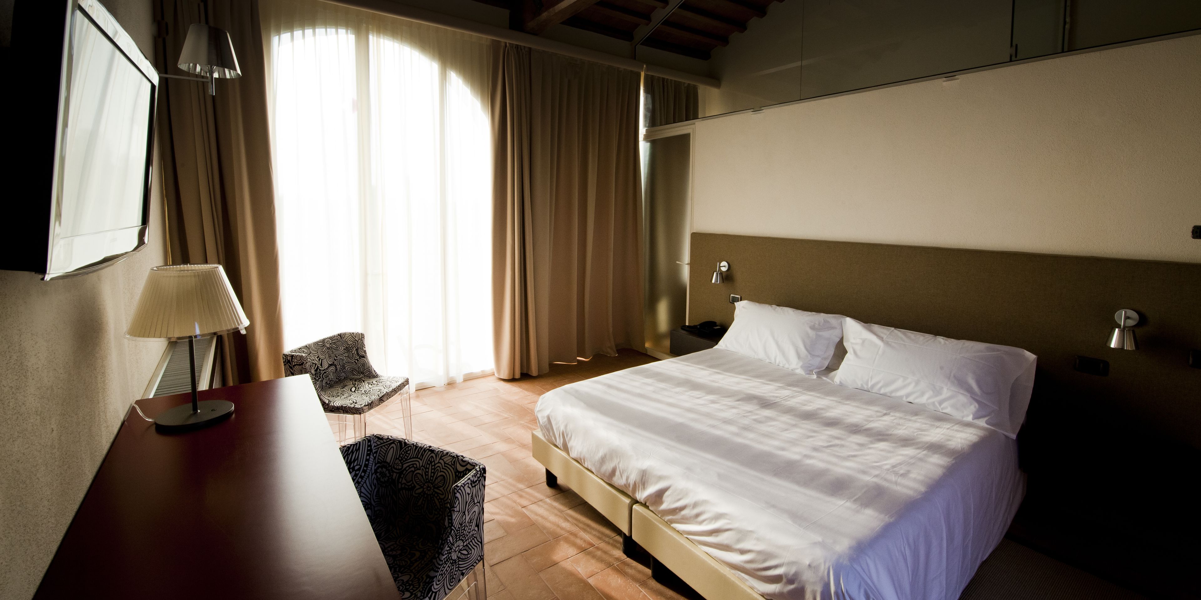 A hotel room with a bed, a desk, a chair, and a lamp.