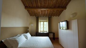 A hotel room with a wooden ceiling, a bed with white linens, a television on the wall, and a window with curtains.