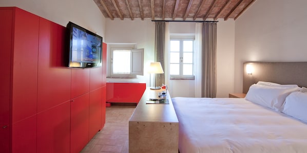 A hotel room with a bed, a desk with a lamp, a TV on the wall, and a red wardrobe. - Locanda Sant'Agata (San Giuliano Terme)