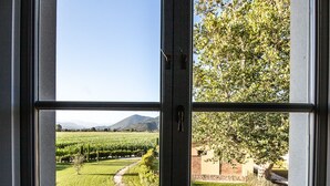 Una habitación con un ventanal que ofrece vistas a un viñedo, un muro de ladrillo y un árbol.