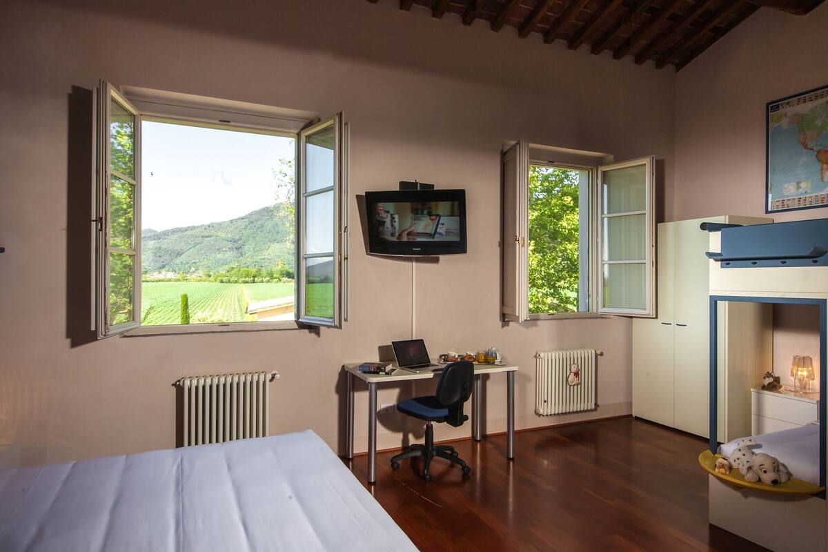 A bedroom with a bed, a desk with a laptop, a TV, and a bunk bed.