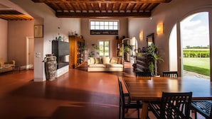 Amplia sala de estar con techo de madera, un ventanal grande, un sofá, una mesa de comedor y una chimenea.